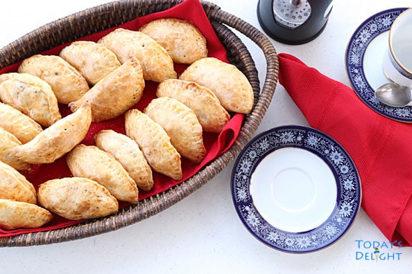 Tray of fried and baked Filipino empanadas on a wooden tray. Saucer, cup for tea and red napkin nearby.