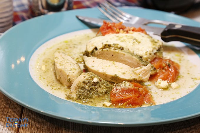 Plated sliced baked pesto chicken breast with fork and knife.