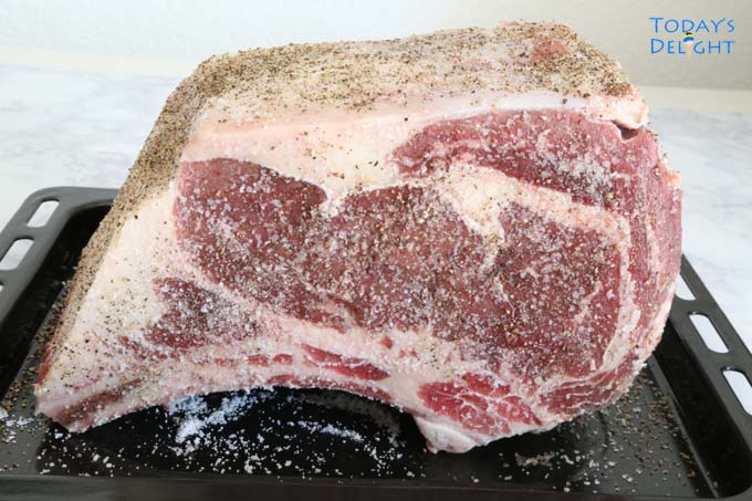 Raw bone-in ribeye roast seasoned with salt and pepper
