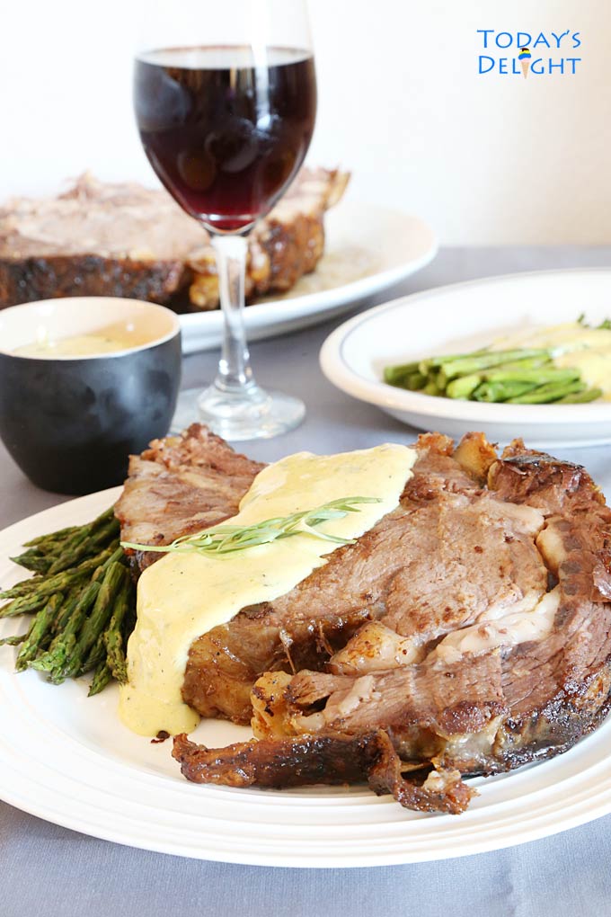 Slice of well-done ribeye roast with sauce and a side of asparagus and a glass of wine.