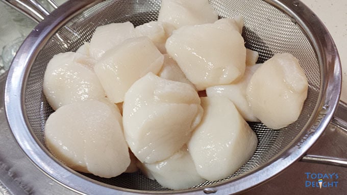 Raw scallops in a collander.