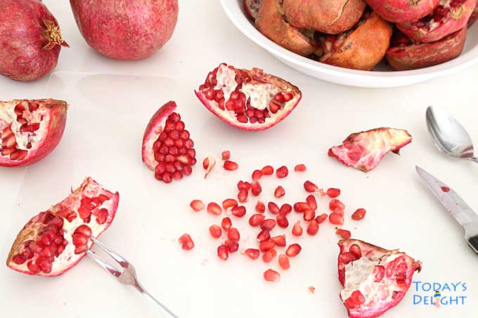 Cracked open pomegranate using a spoon, fork or finger to remove seeds or arils.