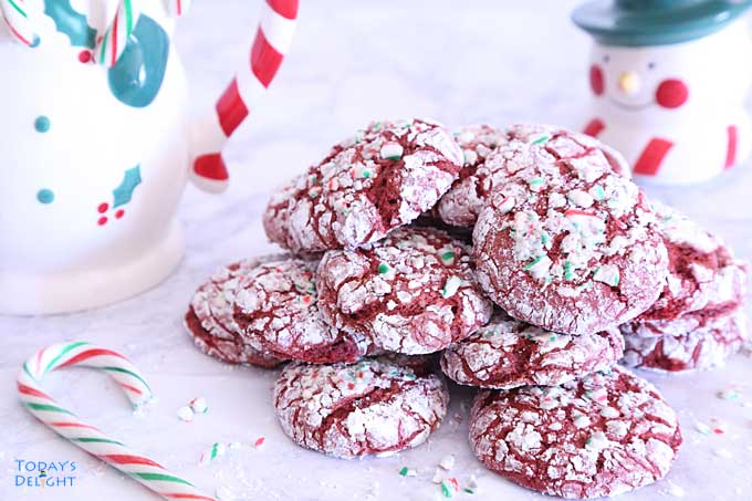 Piled Red Velvet Candy Cane Crinkle Cookies with Snowman jar in the background.
