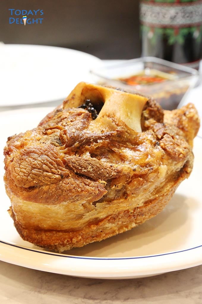Fried pork hock on a plate with a side of spicy vinegar dip and a glass of soda.