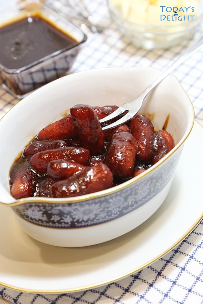 Barbecue little smokies in bowl with a small serving fork, bbq sauce and cheese on the side.