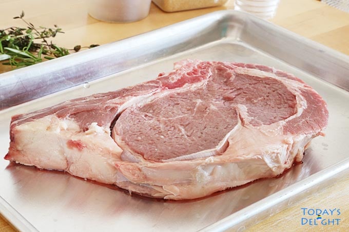 Seasoned ribeye steak on a tray. On the table are thyme and seasonings.