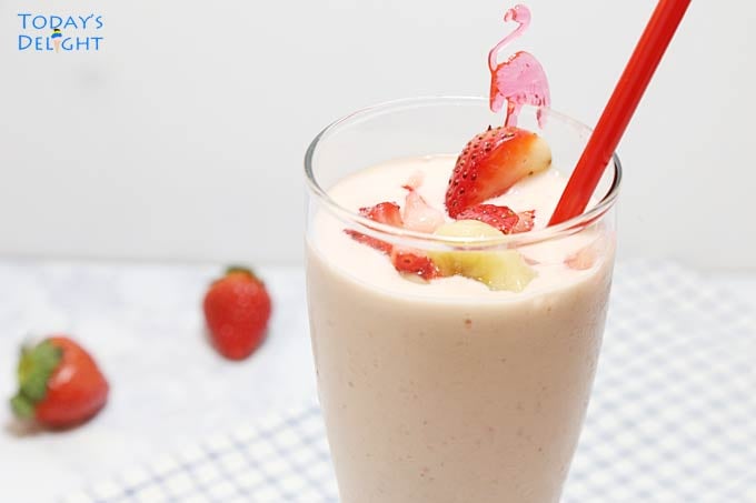 Strawberry banana smoothie garnished with sliced banana and a slice of strawberry with red straw. Background shows two strawberries.