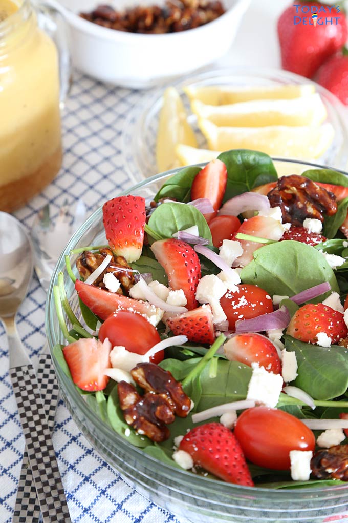 Strawberry spinach salad with candied walnuts, feta, red onions, cherry tomatoes in orange poppy seed dressing in a salad bowl and extra ingredients on the side.
