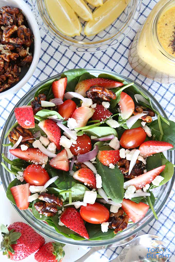 Strawberry spinach salad with candied walnuts, feta, red onions, cherry tomatoes in orange poppy seed dressing in a salad bowl with some ingredients on the side.