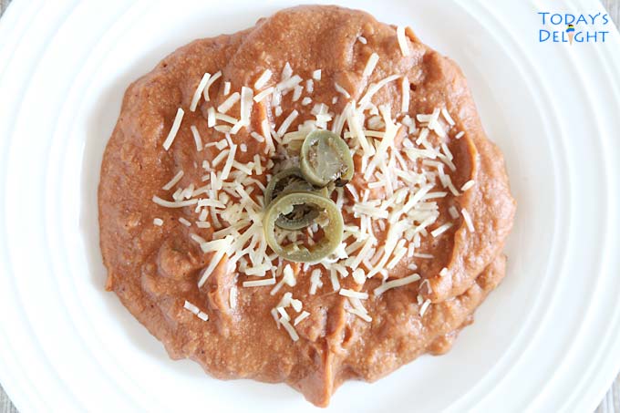 Plated creamy refried beans with grated cheese and jalapenos.