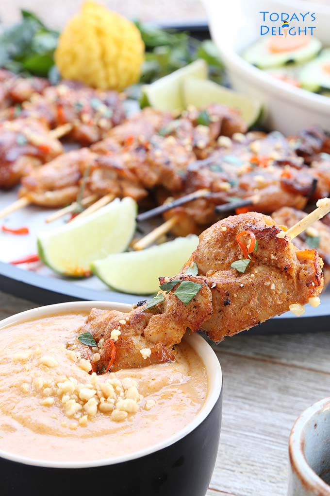 Skewered chicken satay dipped in peanut sauce and a platter of chicken satay with lime wedges and kaffir fruit and cucumber salad.