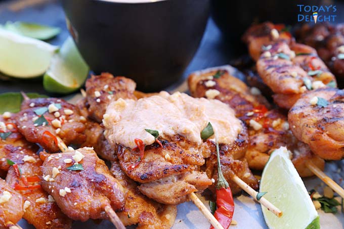 A platter of chicken satay with two skewers with peanut sauce and lime wedges around the platter.