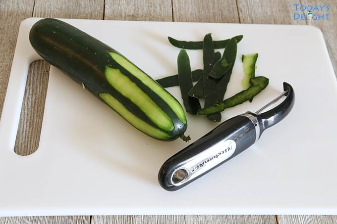 Peeling cucumber with a peeler and a cutting board.