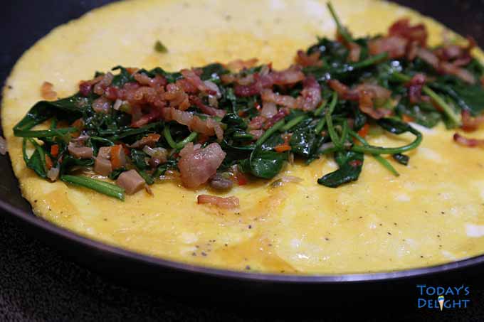Add the vegetable and bacon on top and fold both sides of egg to secure the mixture. Cook for 30 seconds and transfer to a plate.