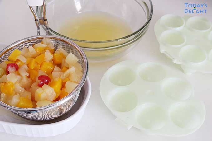Drained fruit cocktail in a strainer and juice in a bowl. Six empty egg molds.