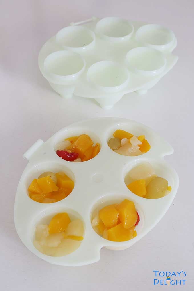 Fill lower half of egg mold with fruit cocktail.