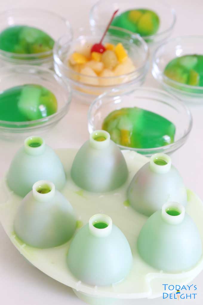 Six egg molds and Easter eggs in small bowls with fruit cocktail.