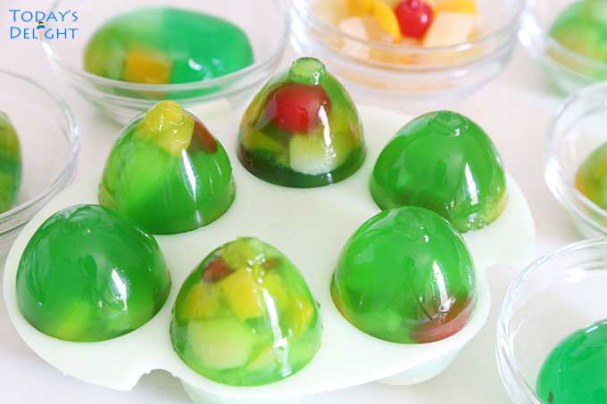 Jello egg jigglers in 6 molds with fruit cocktail and 6 fruit cocktail Easter eggs in small bowls.