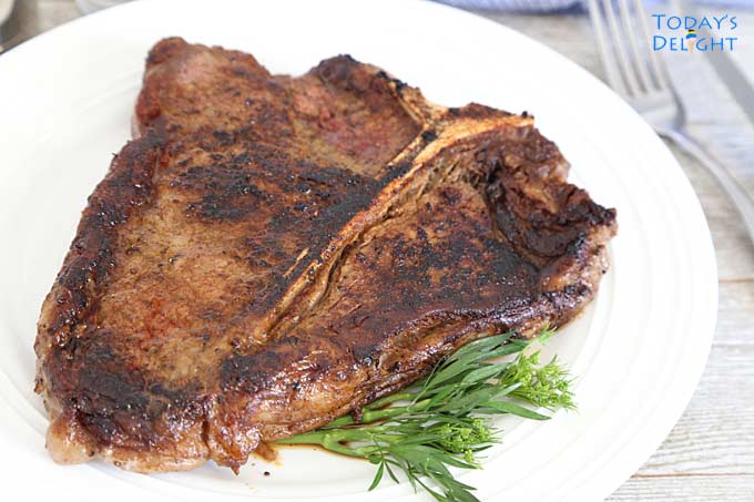 Medium Well Done T-bone steak on a plate with green garnish on the side.