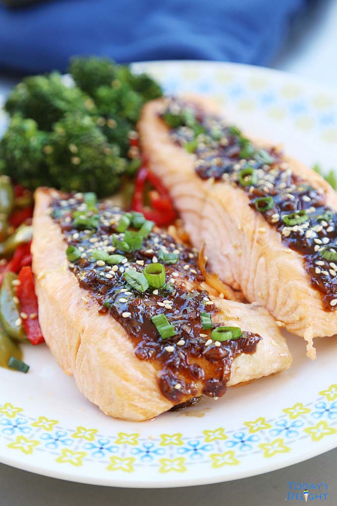 Poached salmon with teriyaki sauce garnished with green onions and sesame seeds and a side of vegetables.