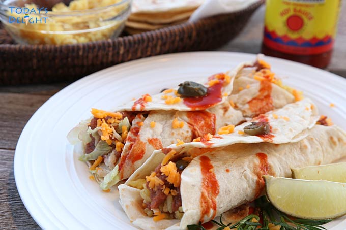 2 burritos in a plate with jalapeno and hot sauce.