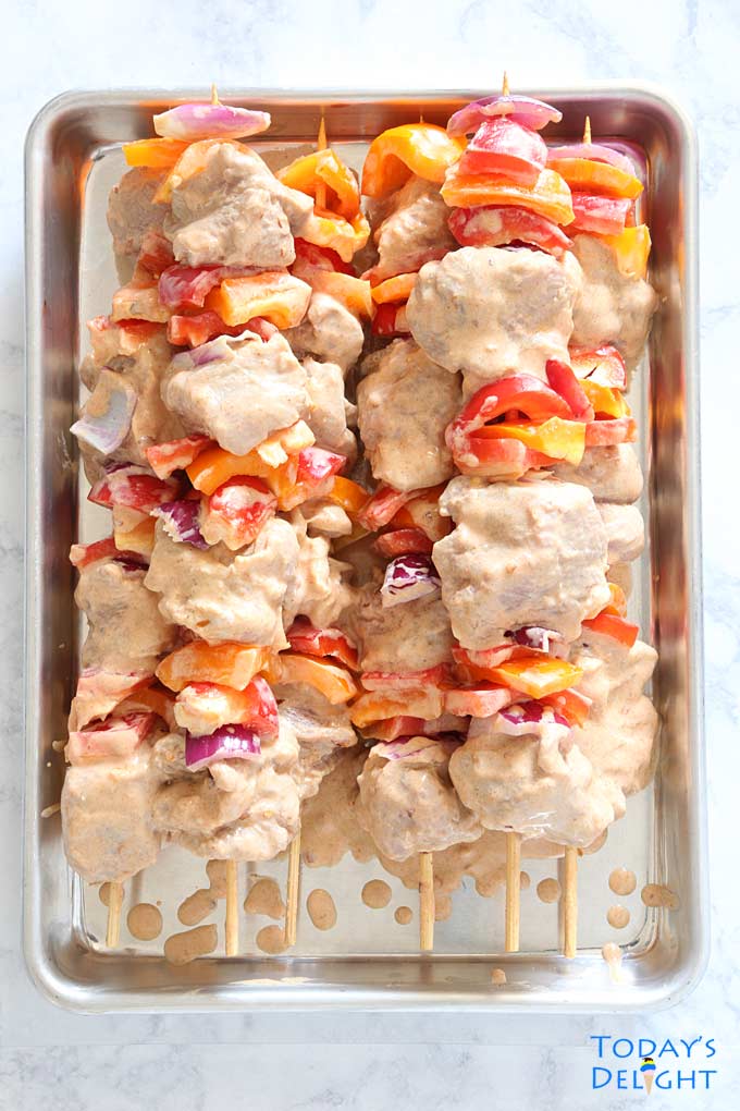 6 skewered pork kabobs with vegetables alternate between pork cubes on a tray.