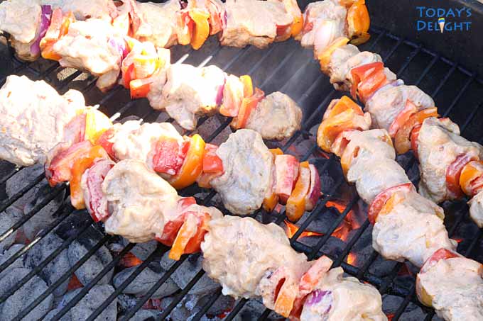 6 pork kebabs cooking on charcoal grill.