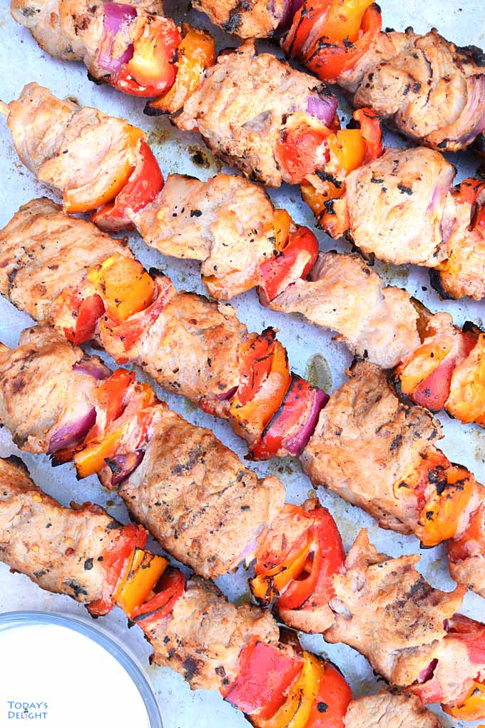 6 skewered Grilled Pork Kabobs with vegetables and dipping sauce on a tray.