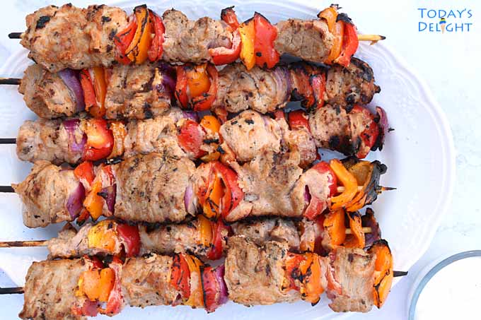 6 skewers of juicy, tender grilled pork kabobs on a platter and a dipping sauce on the side.
