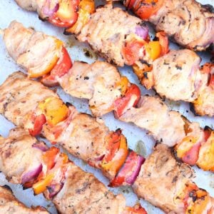 Six skewered pork kabobs with bell peppers and red onion on a tray.