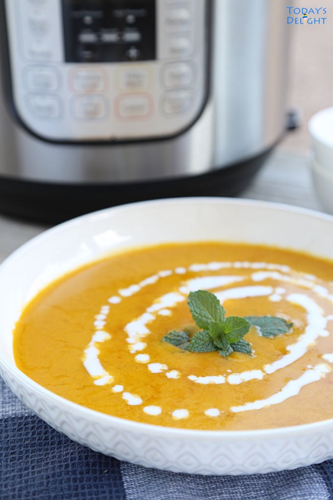 Kabocha squash soup garnished with mint leaves at the center and a swirl of coconut milk around the mints leaves. On the background is an instant pot and 2 bowls with spoons.