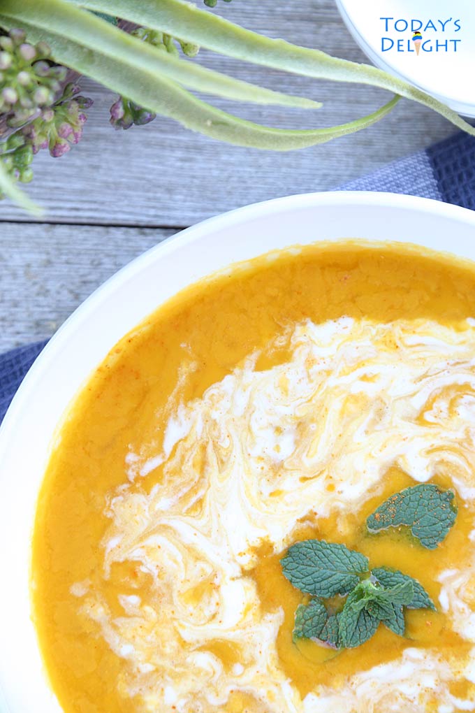 Creamy kabocha squash soup garnished with mint leaves and a swirl of coconut milk. A vase and bowl on the side.