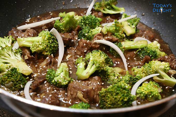 Cooked beef and broccoli stir fry in a skillet garnished with sesame seeds and onion.