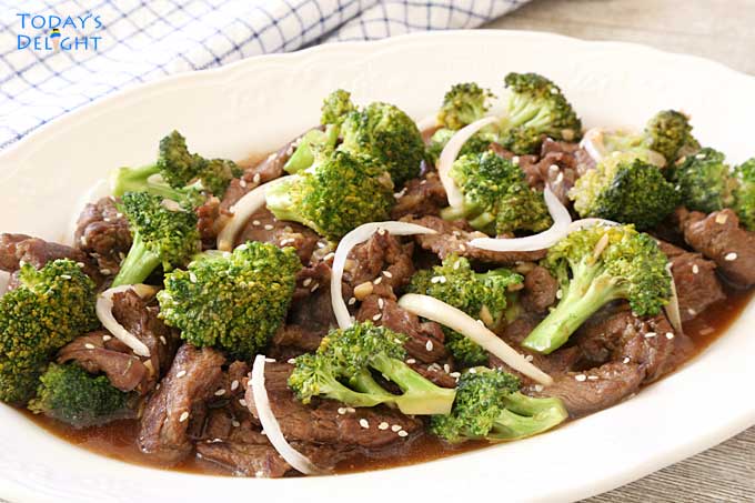 Easy beef and broccoli stir fry garnished with sesame seeds and julienned onion in a serving plate. A napkin nearby.