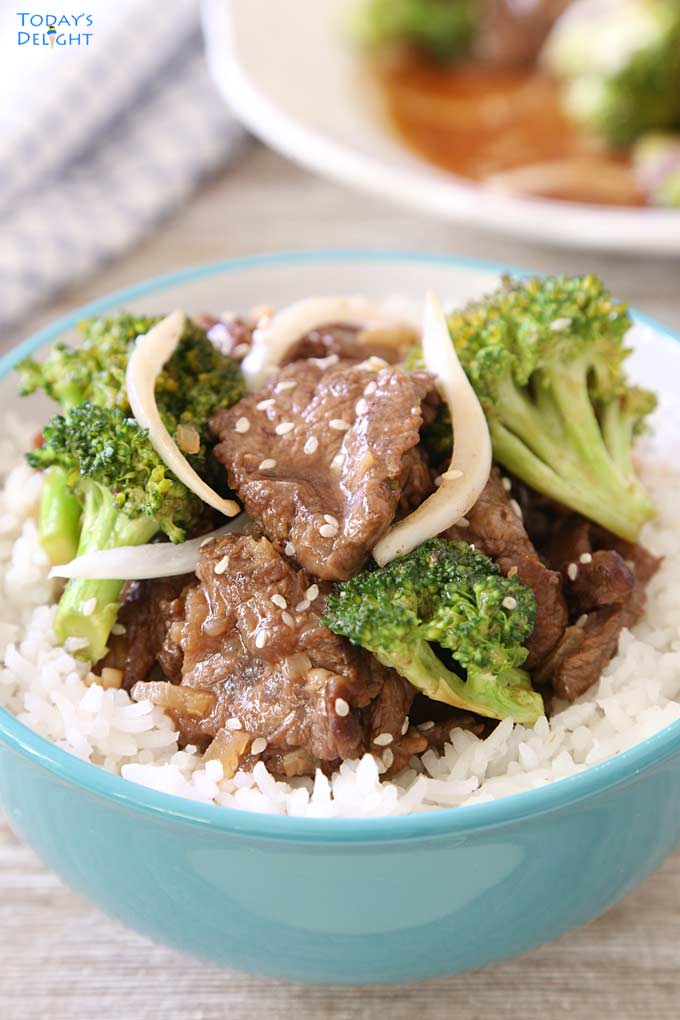 Beef and broccoli stir fry in a bowl garnished with onion and sesame seeds. One more serving of stir fry and a napkin in the background.