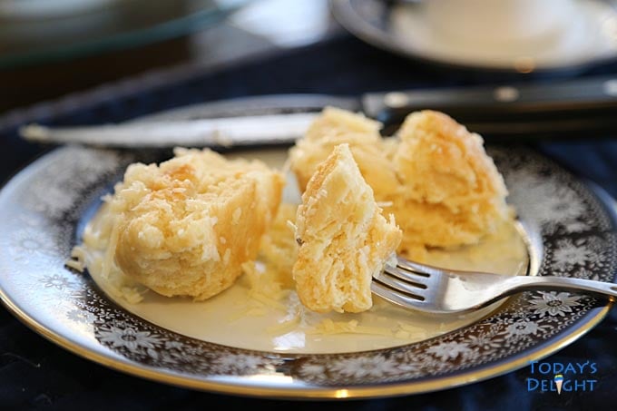 Ensaymada cut with a knife on a plate and eating with a fork. A cup of coffee on the side.