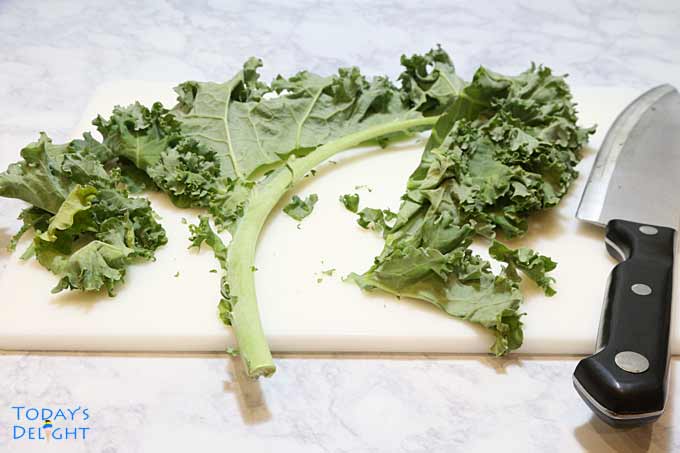 Cutting kale leaves with a knife on a cutting board.