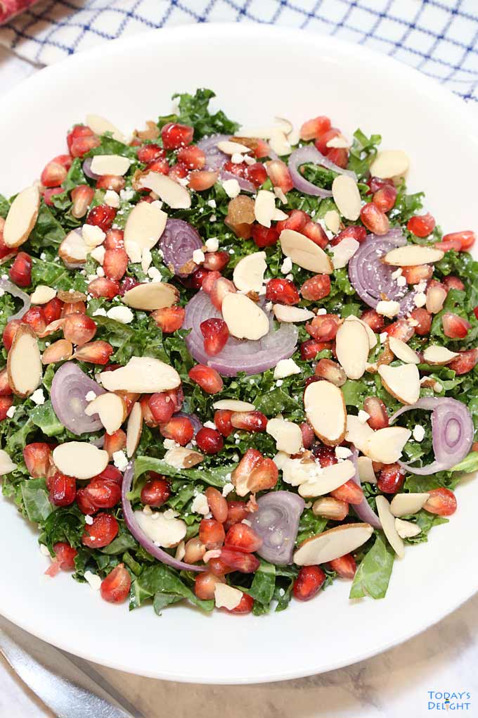 Pomegranate Kale Salad with shallots, feta cheese, and shaved almonds in bowl.