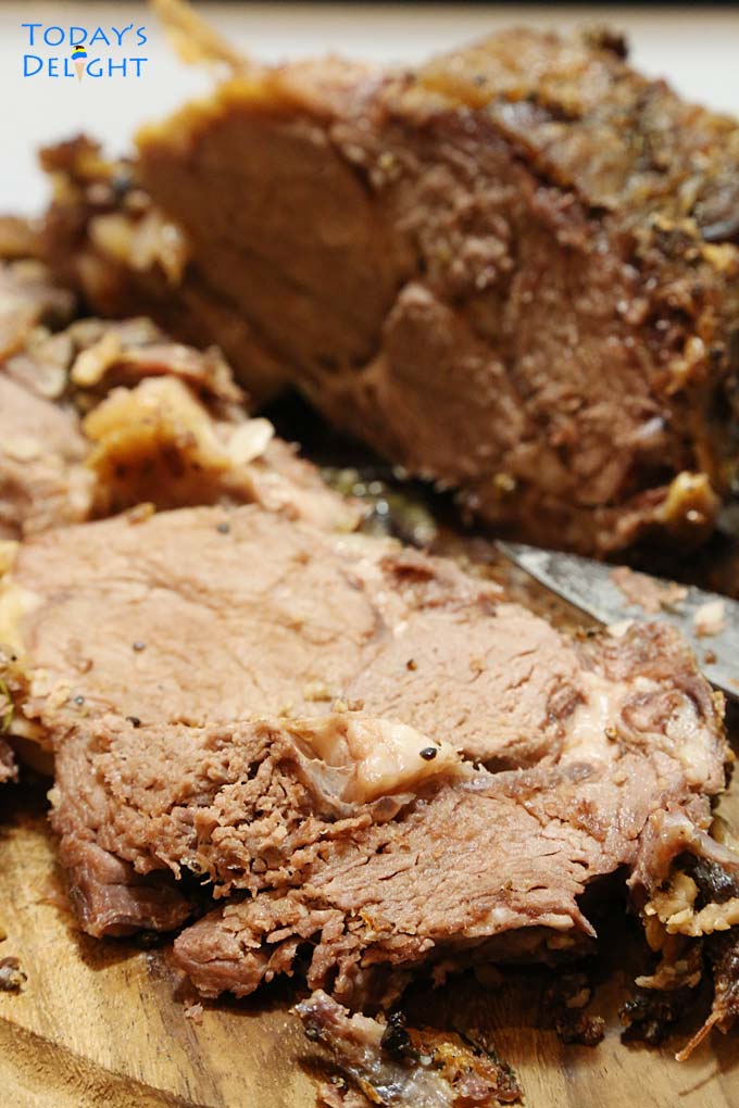 A slice of medium-well done rib roast on a cutting board, a knife and the whole rib roast.