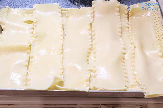 Cooked lasagna noodles are in a tray that is lightly sprayed with olive oil.
