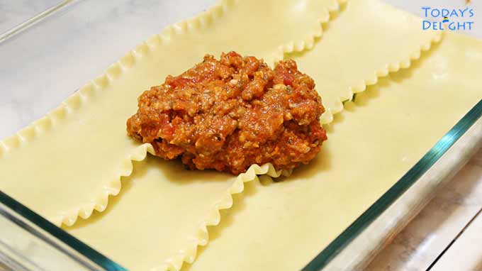 Lasagna noodles and meat sauce are added in the casserole pan.