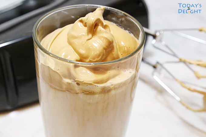 A Glass of cold Whipped Coffee AKA Dalgona Coffee and hand mixer.