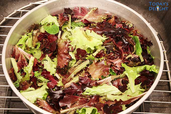 Mixed greens submerged in water in a big bowl.