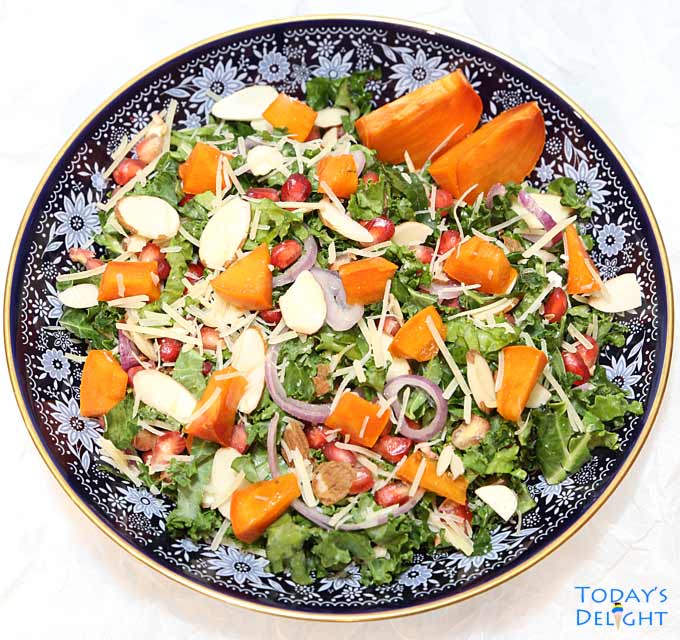 Persimmon Pomegranate Salad with kale, red onions, shaved almonds, parmesan cheese in pomegranate honey vinaigrette on a plate.