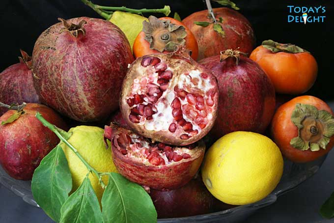 Persimmons, pomegranates, and lemons on a fruit tray.