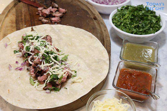 Flank steak and other ingredients on flour tortilla to make beef burrito.