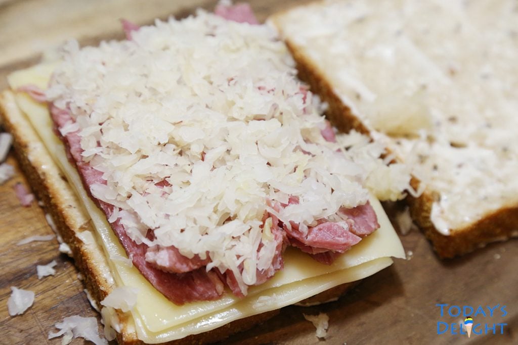 2 breads, one with corned beef, cheese, sauerkraut and garlic aioli.