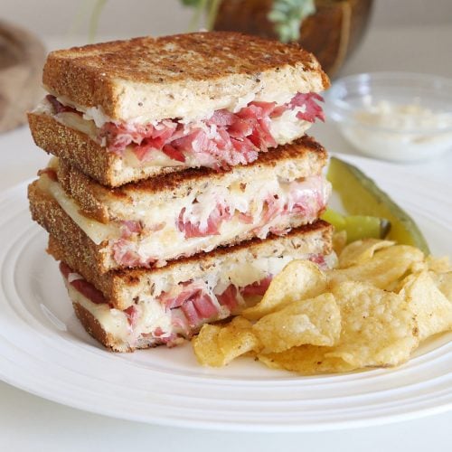 A side of chips and dill spears served with reuben sandwich with garlic aioli.