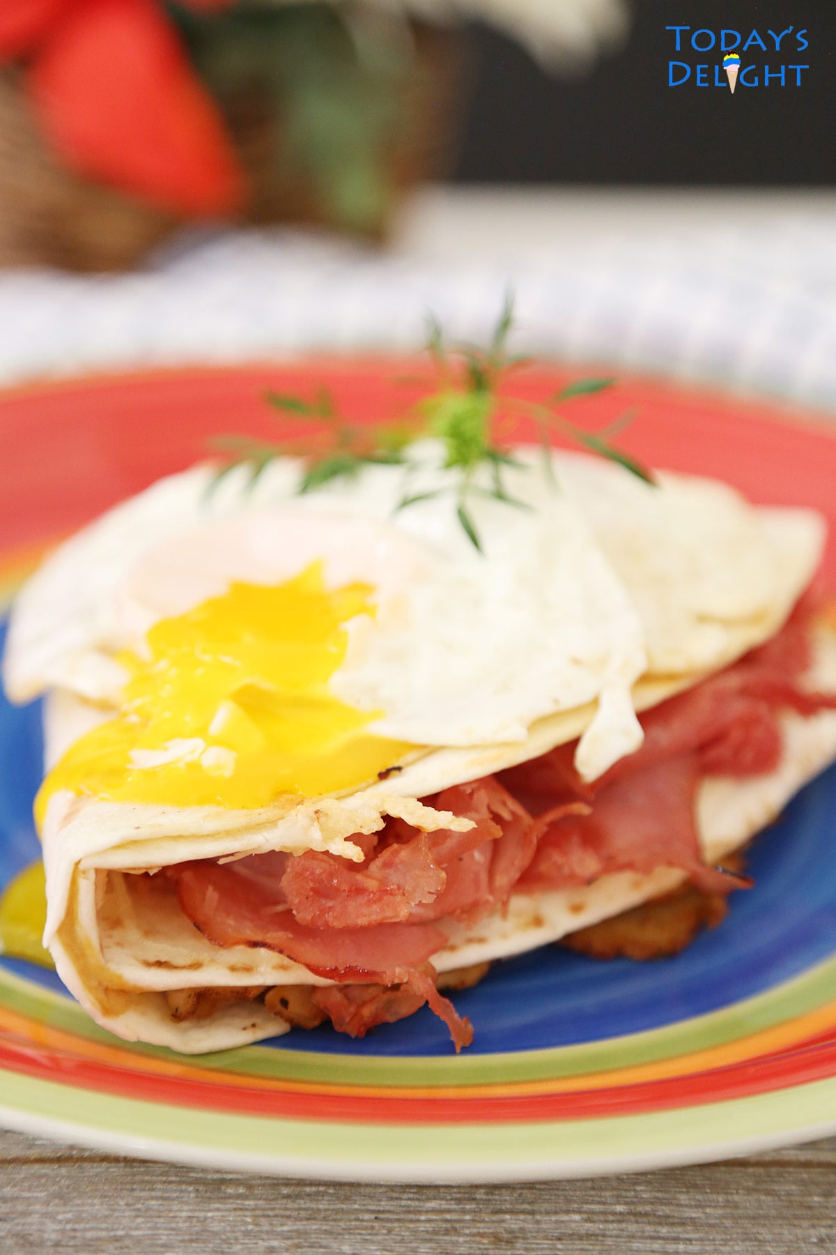 Broken over easy egg yolk over on top of Monte Cristo Sandwich in tortilla wrap on a plate.