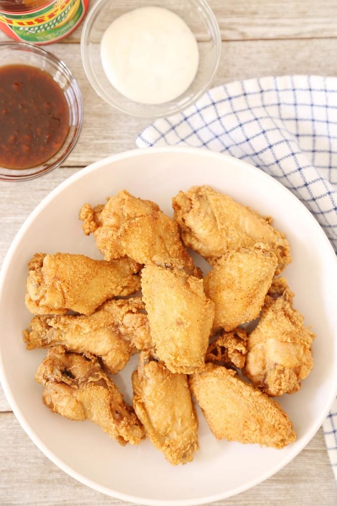Crispy Patis Fried Chicken Wings in a plate with a side of blue cheese dressing, sweet and spicy sauce and ketchup.
